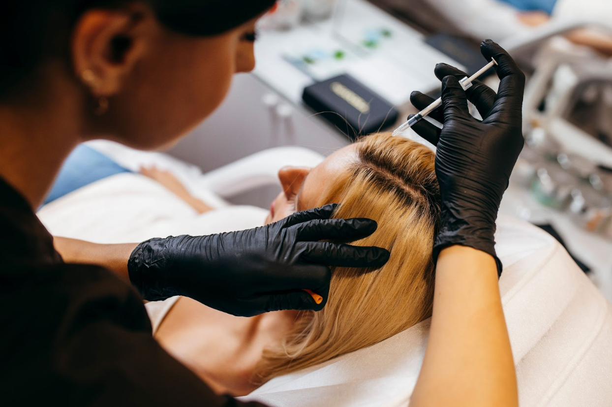 A professional performing PRP hair treatment on a blonde woman by injecting platelet-rich plasma into her scalp to stimulate hair growth and improve thickness.