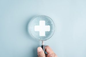 Hand holding magnifying glass with white medical cross and hexagonal molecular patterns, representing peptide therapy safety research and medical oversight