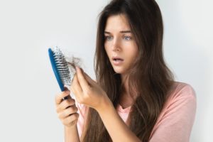 Woman shocked by hair loss while brushing, exploring PRP vs. PRF treatments for natural hair restoration