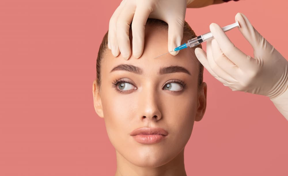 Woman receiving forehead injection during wrinkle treatment, illustrating Xeomin vs. BOTOX options for smoother, youthful skin results.